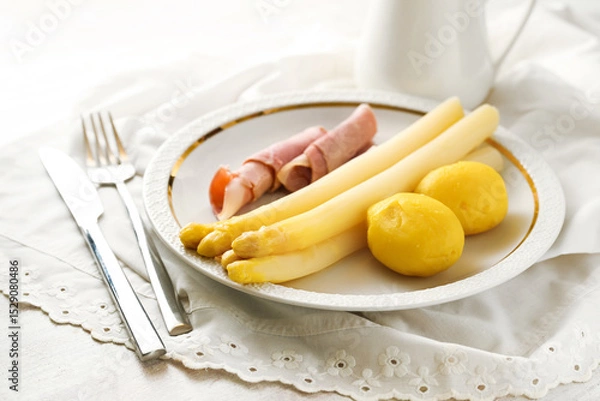 Fototapeta White asparagus, potatoes and boiled ham on a white plate with napkin and cutlery, traditional, seasonal meal, copy space, selected focus