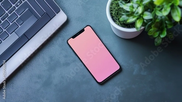 Fototapeta Modern smartphone with pink blank screen lying on textured gray desk alongside a keyboard and potted green plant, emphasizing technology and workspace setup