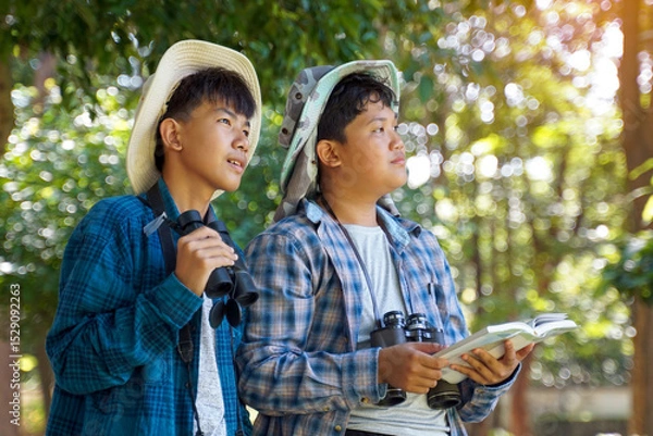 Fototapeta Two Asian boys use binoculars to study the local birds in a community forest. Soft and selective focus.