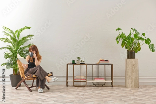 Obraz A woman is reading a book at home, looking at the phone and tablet. Decorative interior style and vase of plant.