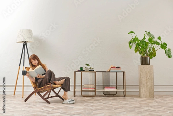 Obraz A woman is reading a book at home, looking at the phone and tablet. Decorative interior style and vase of plant.