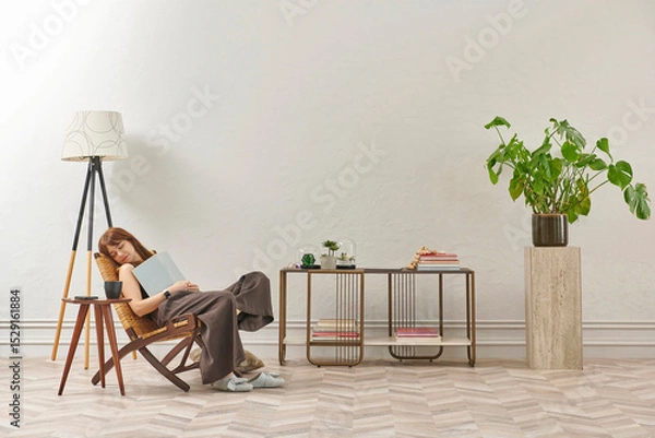 Obraz A woman is reading a book at home, looking at the phone and tablet. Decorative interior style and vase of plant.