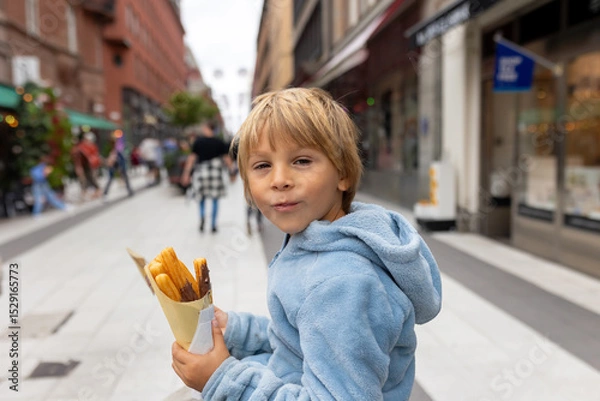 Obraz Cute blond child, eating churros on the street in the city of Stockhlom, sweet desert sold on every corner