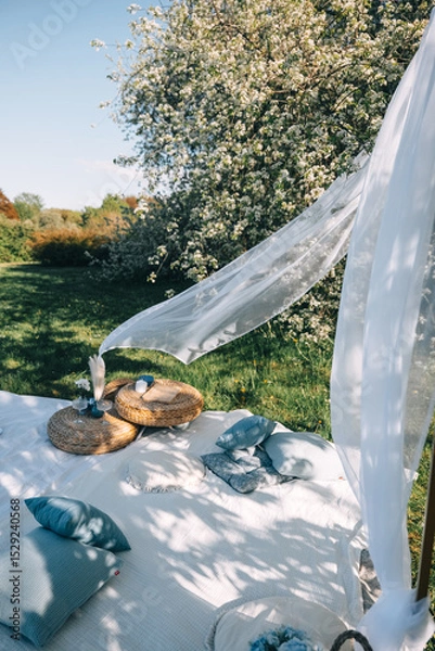 Fototapeta Cozy outdoor seating area with pillows and decor near blooming trees on a sunny day