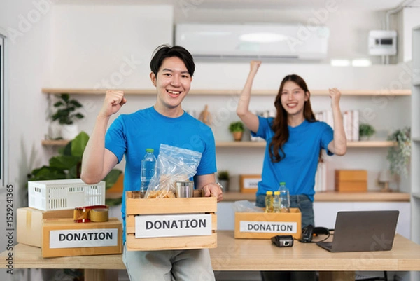 Obraz Donation and Community Support. Young volunteers celebrating successful food drive in a modern workspace.
