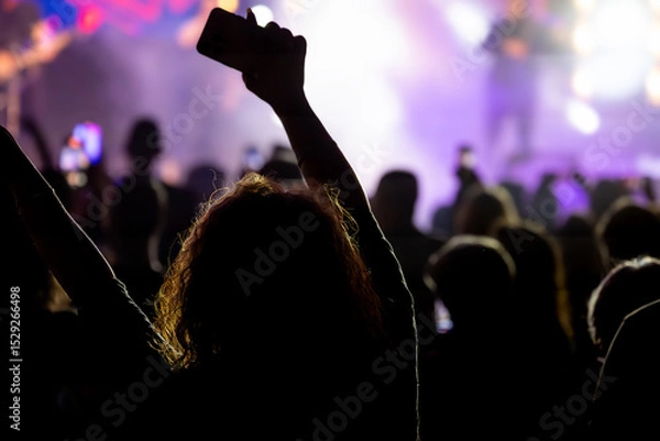 Fototapeta The audience gets excited and cheers with their arms raised during the concert of the musical band that performs on stage.