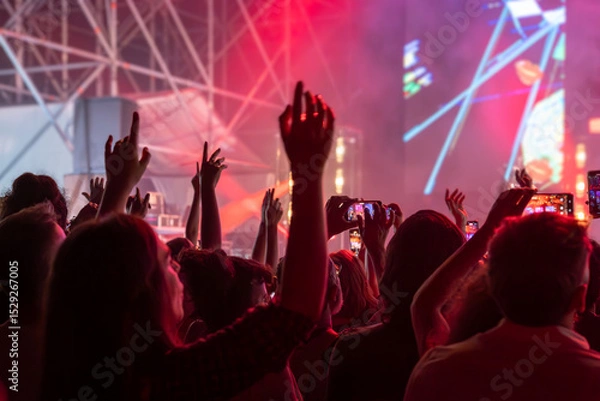 Fototapeta The audience gets excited and cheers with their arms raised during the concert of the musical band that performs on stage.