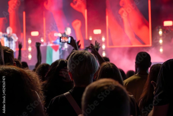 Fototapeta The audience records videos and takes photos with their smartphones during the concert of the musical band that performs on stage.