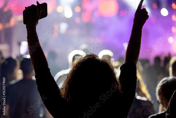 Fototapeta The audience gets excited and cheers with their arms raised during the concert of the musical band that performs on stage.