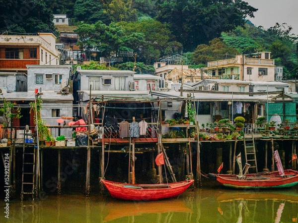 Fototapeta Traditional Stilt Houses In Hong Kong Village: Colorful Weathered Structures Built On Wooden Pilings Amid Urban Surroundings And Mountain Backdrop In Southeast Asia
