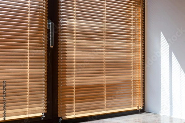 Obraz Sunlight filters through wooden blinds 25 mm, casting bright striped shadows on the windowsill and wall. The natural wood slats create warm, cozy ambiance while controlling light and privacy indoors.