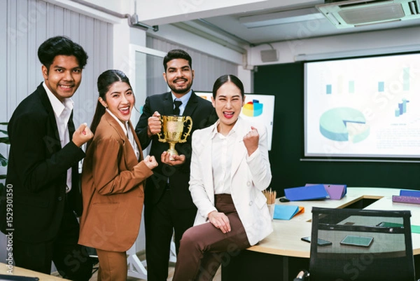 Fototapeta Diverse business team celebrates corporate success with a trophy in a modern office. Charts on screen suggest teamwork, achievement, and strategic consulting in a thriving work environment.