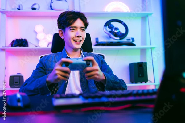 Fototapeta Young man enthusiastically playing video games at home with a game controller, surrounded by neon lighting and modern gear. Ideal for themes of gaming, streaming, fun, and esports lifestyle.