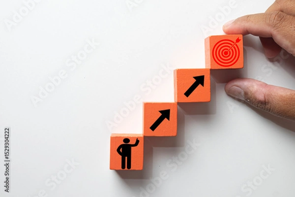Obraz Hand arranging wooden blocks in steps, from a person icon to a target goal. Concept for business growth, career path development, achieving objectives,personal development, ambition, self-improvement.