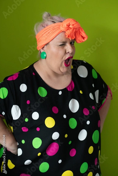 Fototapeta Plus size woman in vibrant polka dot outfit making a comic shrug gesture with outstretched hands and amusing expression.