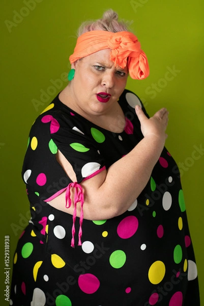 Fototapeta Plus size woman in vibrant polka dot outfit making a comic shrug gesture with outstretched hands and amusing expression.
