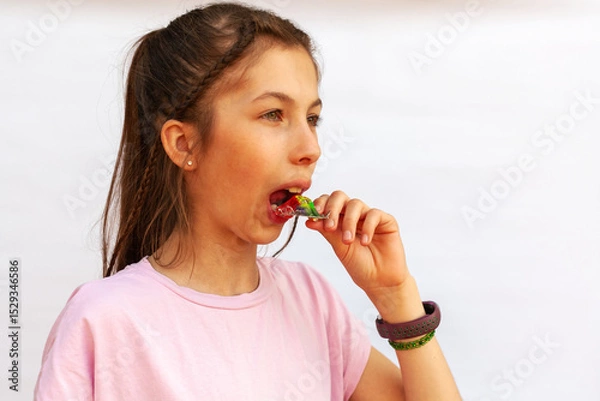 Fototapeta Young girl in pink t-shirt putting orthodontic plate on teeth with uneven teeth, malocclusion on white background. Concept orthodontic treatment