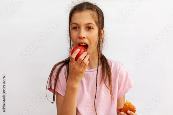 Fototapeta Girl in pink t-shirt holds in one hand delicious croissant and in the other hand red apple on white background. Healthy eating concept