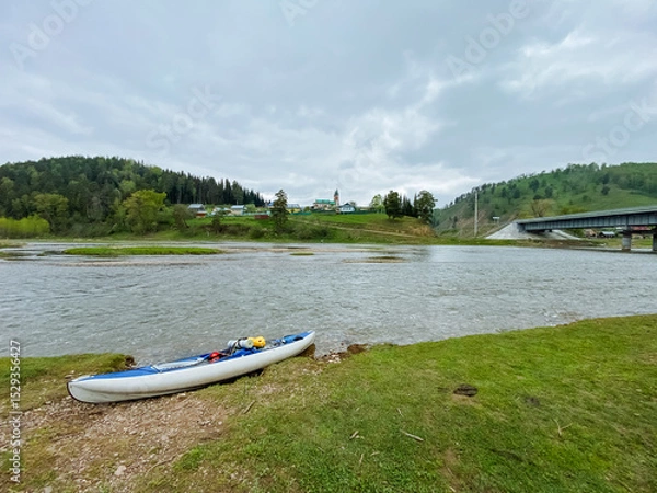 Obraz A beautiful white kayak is peacefully sitting on the sandy shore of a serene lake, resting quietly next to the gentle, glistening water that reflects the surrounding landscape