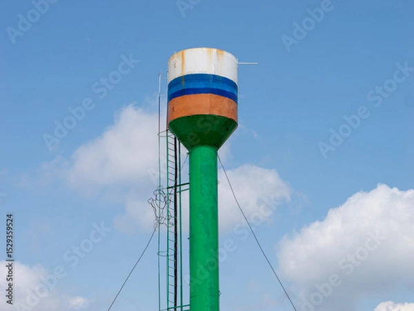 Fototapeta A tall green and blue water tower with a ladder on top