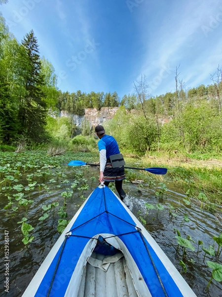 Obraz A skilled man gracefully paddles a vibrant blue and white kayak along a tranquil river, savoring the breathtaking scenery and the exhilarating thrill of his exciting outdoor adventure