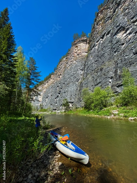 Obraz A blue and white kayak sits gracefully on the sandy shore of a beautiful river, ready to embark on an exciting adventure across the waters surface, inviting all to enjoy its splendor
