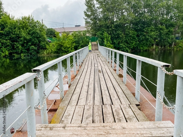 Obraz A beautifully crafted wooden bridge spans a calm body of water, surrounded by lush greenery and vibrant trees, creating a stunning natural backdrop that enhances the scene