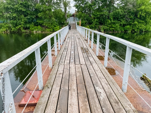 Obraz A beautifully crafted wooden bridge spans gracefully over a serene body of water, with lush trees thoughtfully positioned in the background, enhancing the picturesque view