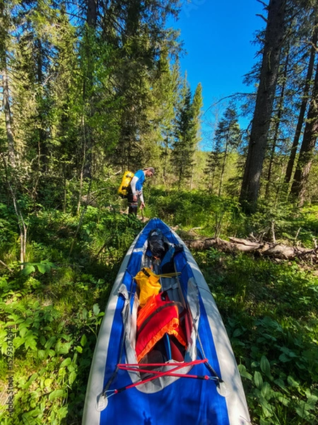Obraz A joyful person stands beside a vibrant, colorful kayak in the lush woods, surrounded by tall, majestic trees, eagerly anticipating an exciting outdoor adventure on the serene water surface