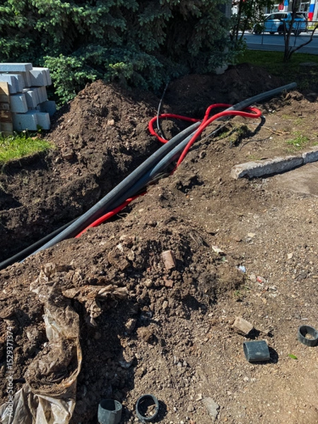 Obraz A chaotic mess of electrical wires is haphazardly scattered in the dirt, looking extremely disorganized and untidy, likely due to recent construction or repair work taking place nearby