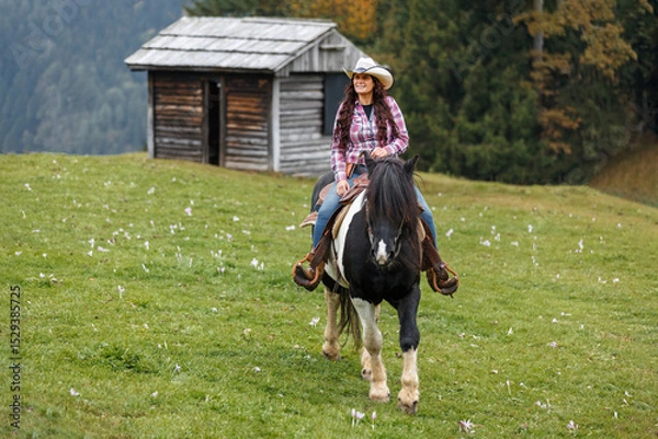 Fototapeta Authentic western scene of a confident cowgirl on horseback, riding through scenic mountain terrain under a light mist