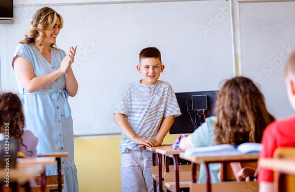 Obraz Smiling teacher assisting young boy with assignment at school.