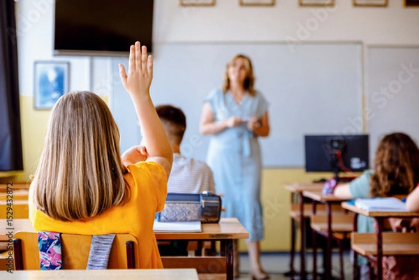 Obraz Rear view of girl raising hand to answer teacher's question during class in classroom.