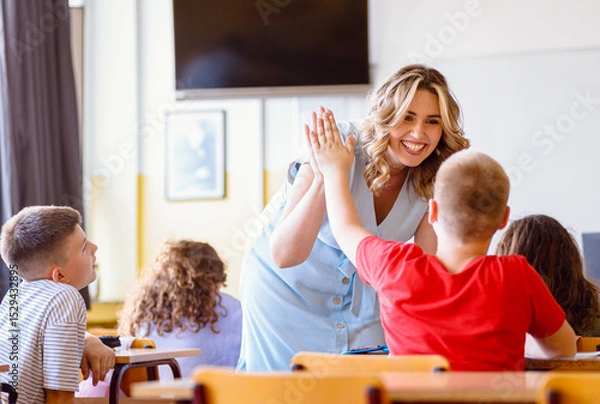 Obraz Smiling teacher assisting young boy with assignment at school desk in classroom.