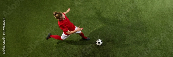 Fototapeta aerial view of female football player stretching to kick ball from above view with dynamic motion on green grassy playground with copy space. Banner. Concept of sport, strength, tournament, energy