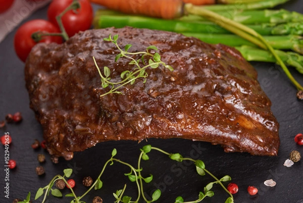 Fototapeta Pork roasted, grilled spare ribs from a summer BBQ served with Vegetables, asparagus, baby carrots, fresh tomatoes and  spices. smoked ribs on black stone background. top view,