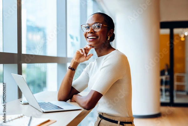 Fototapeta Smiling professional seated at a desk with a laptop in an office