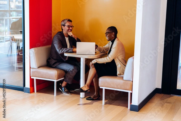 Fototapeta Two professionals discussing ideas on a laptop in a bright office booth