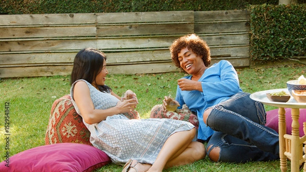 Obraz Two Smiling Mature Female Friends Enjoying Drinks And Snacks In Backyard Garden Together