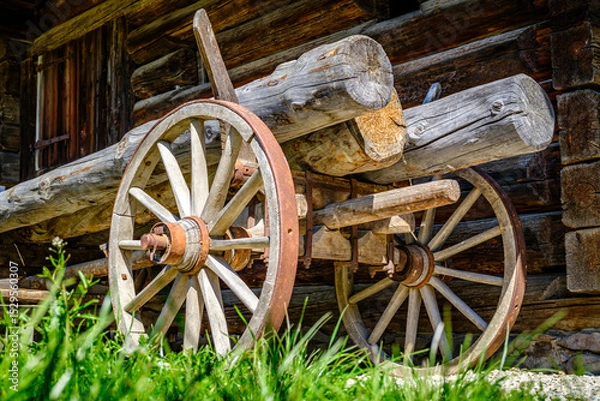 Fototapeta Vintage wooden cart with large wheels resting on a dusty floor in a rustic barn environment during the late afternoon light