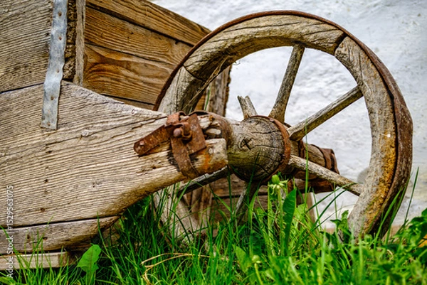 Fototapeta Vintage wooden cart with large wheels resting on a dusty floor in a rustic barn environment during the late afternoon light