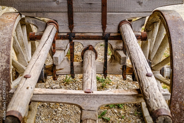 Fototapeta Vintage wooden cart with large wheels resting on a dusty floor in a rustic barn environment during the late afternoon light