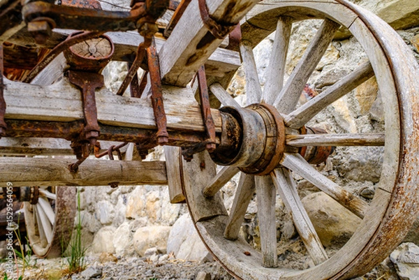 Fototapeta Vintage wooden cart with large wheels resting on a dusty floor in a rustic barn environment during the late afternoon light