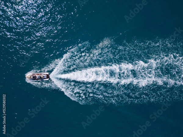 Fototapeta Aerial view of a jet ski speeding across dark blue water, leaving a dynamic white trail. Captured by drone from above, showcasing motion, power, and summer fun on the sea
