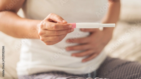 Fototapeta A woman holding a pregnancy test. She is smiling and she is happy about the result