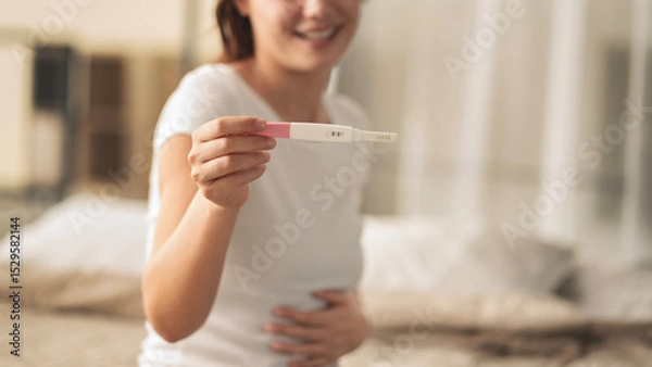 Fototapeta A woman holding a pregnancy test. She is smiling and she is happy about the result