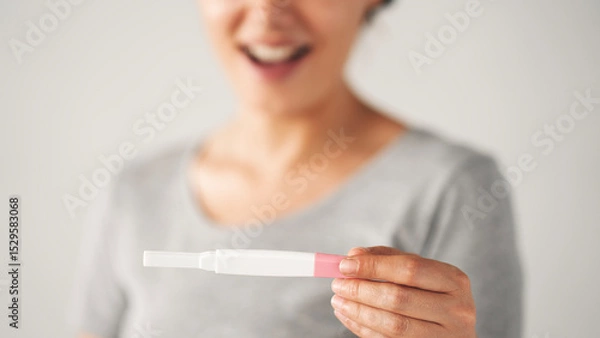 Fototapeta A woman holding a pregnancy test. She is smiling and she is happy about the result