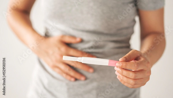 Fototapeta A woman holding a pregnancy test. She is smiling and she is happy about the result