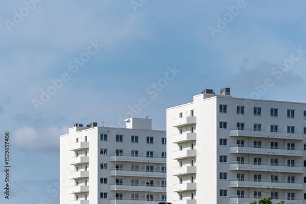Fototapeta Modern residential buildings with clean lines and white facades rise into the sky. The sky is slightly cloudy.