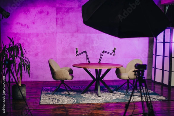 Fototapeta Engaging podcast setup featuring a modern round table with microphones and comfortable chairs in a vibrant studio environment
